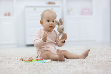 Photo of Cute little baby with rattles on floor indoors