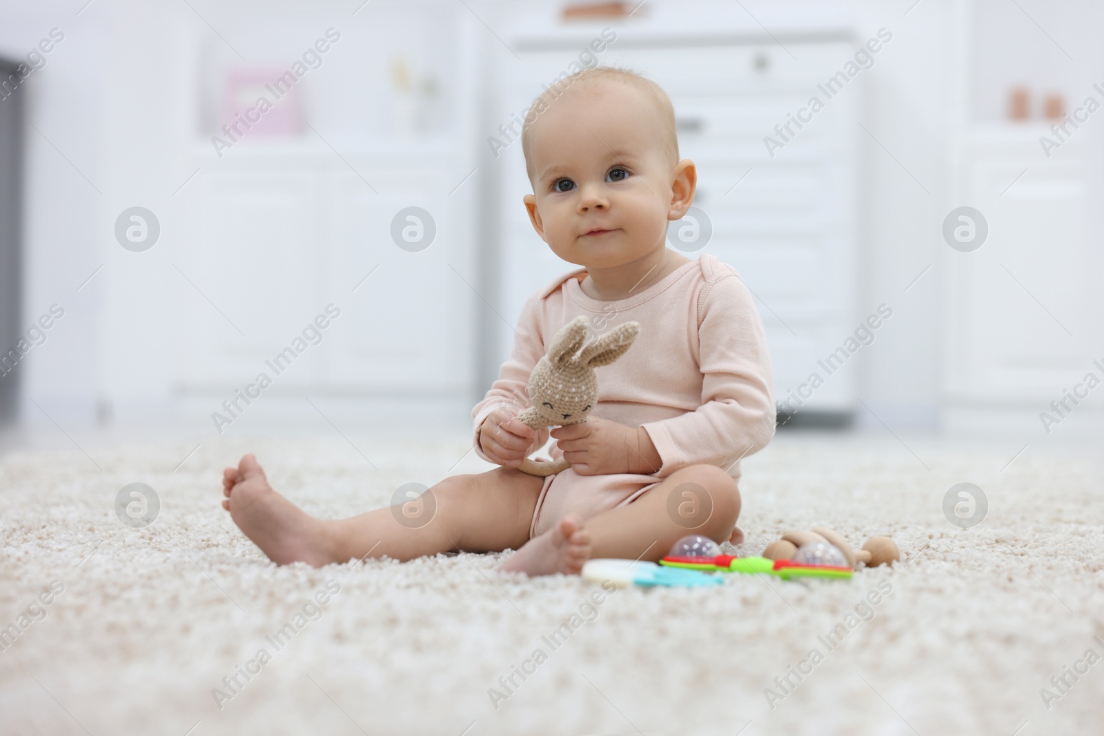 Photo of Cute little baby with rattles on floor indoors