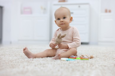 Photo of Cute little baby with rattles on floor indoors