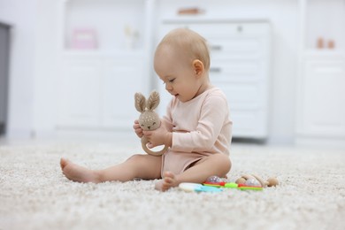 Photo of Cute little baby with rattles on floor indoors