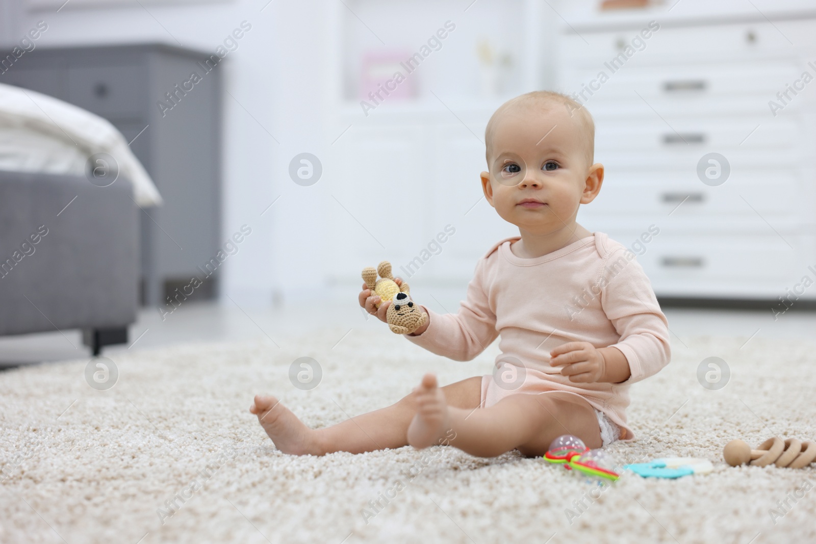 Photo of Cute little baby with rattles on floor indoors, space for text