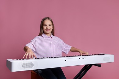 Photo of Cute girl playing synthesizer on pink background