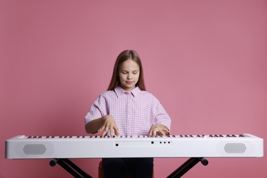 Photo of Cute girl playing synthesizer on pink background