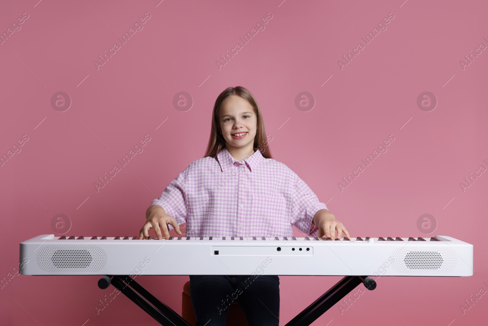 Photo of Cute girl playing synthesizer on pink background