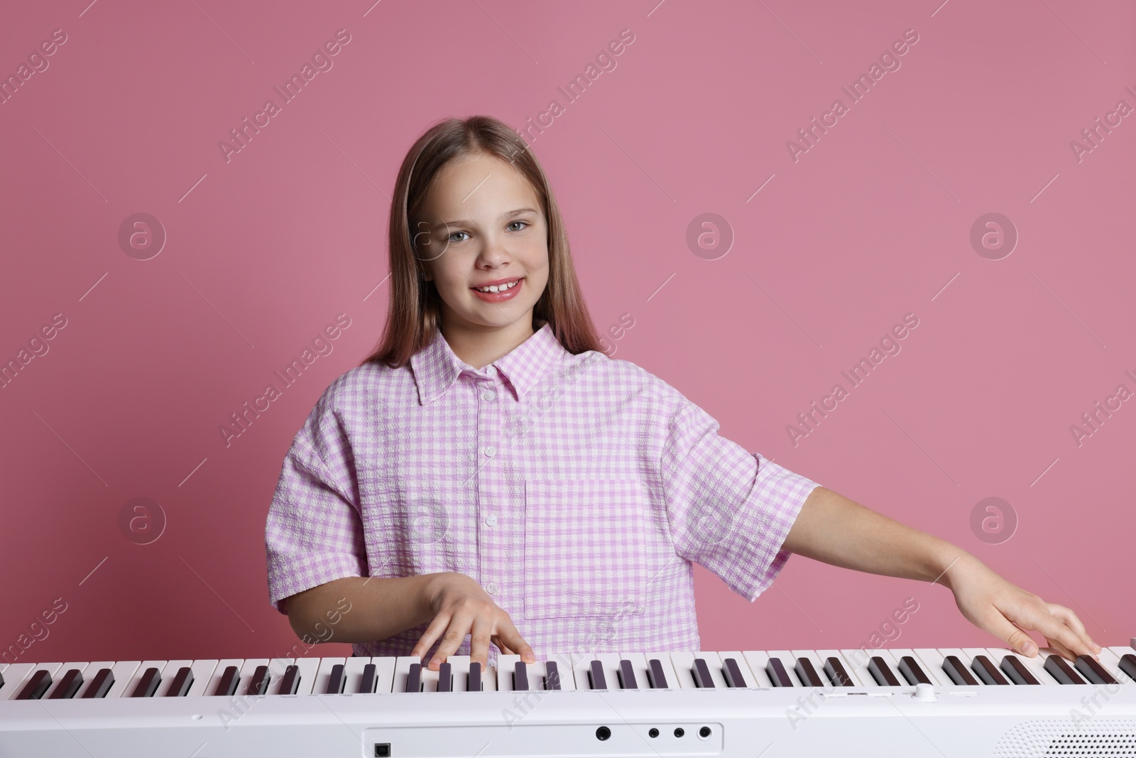 Photo of Cute girl playing synthesizer on pink background