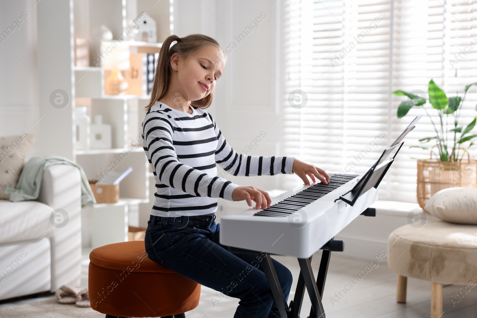 Photo of Cute girl playing synthesizer at home. Electronic musical instrument