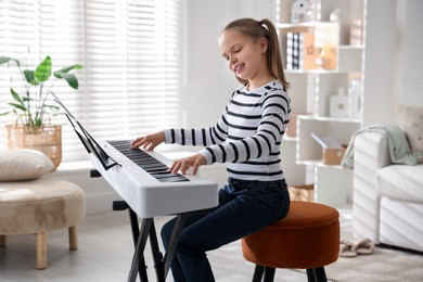 Photo of Cute girl playing synthesizer at home. Electronic musical instrument