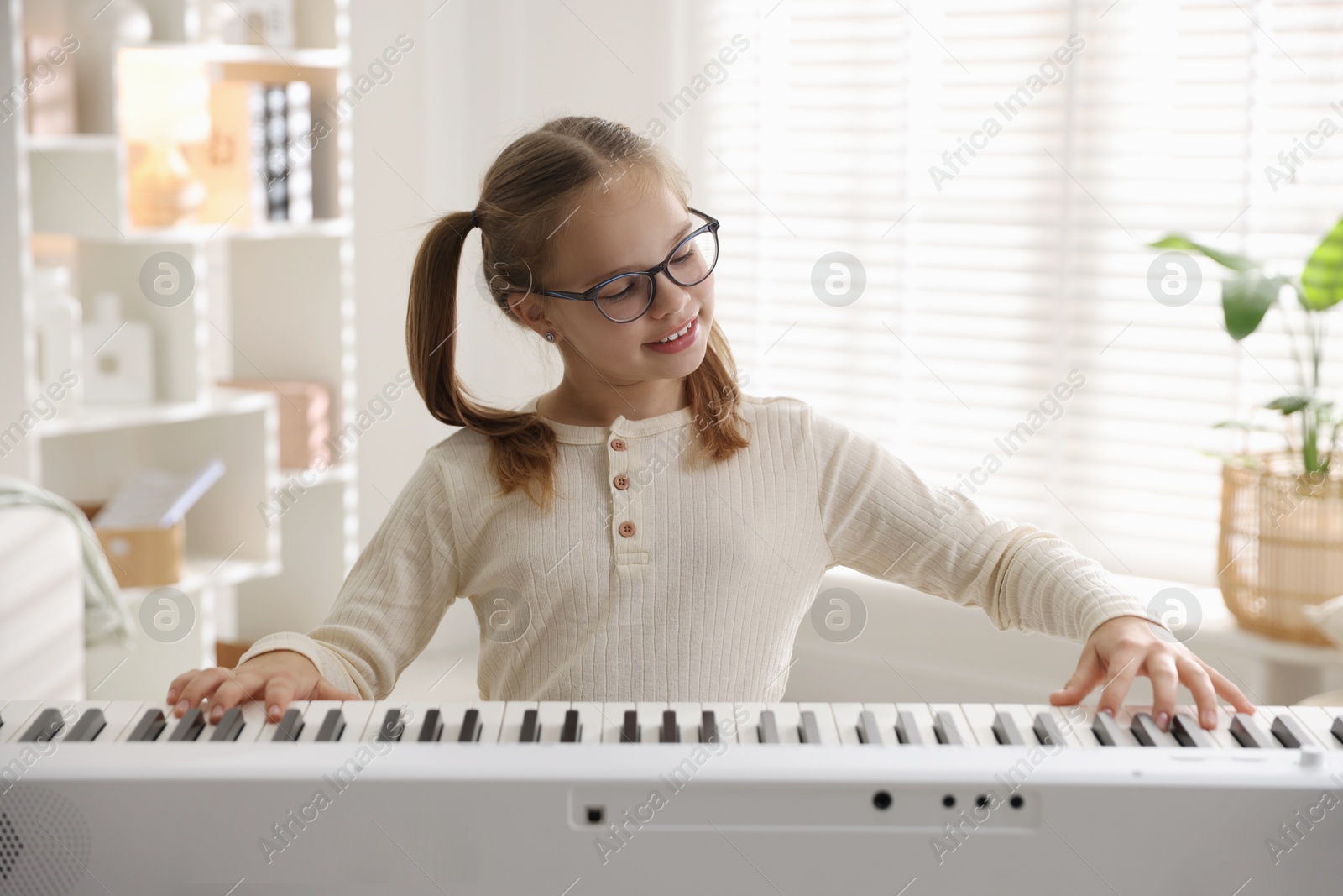 Photo of Cute girl playing synthesizer at home. Electronic musical instrument