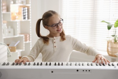 Photo of Cute girl playing synthesizer at home. Electronic musical instrument