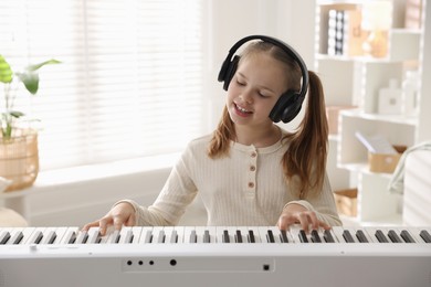 Photo of Cute girl in headphones playing synthesizer at home