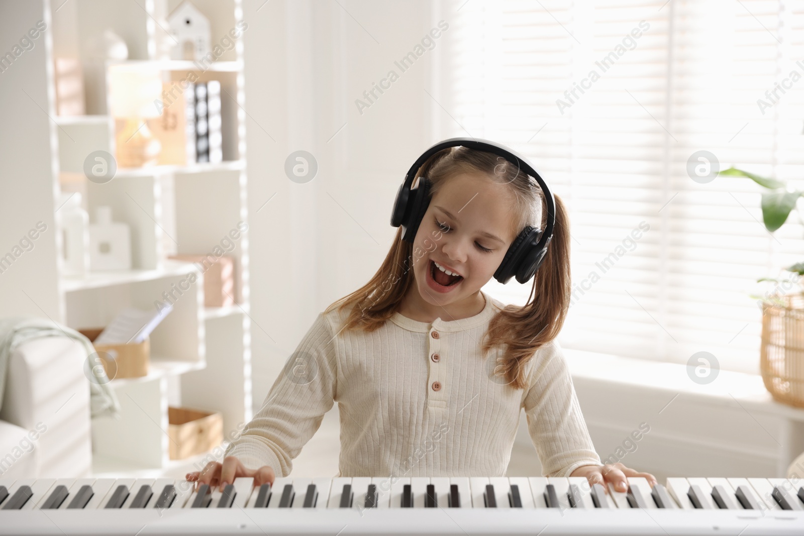 Photo of Cute girl in headphones playing synthesizer at home