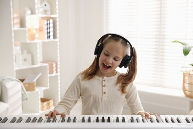 Photo of Cute girl in headphones playing synthesizer at home