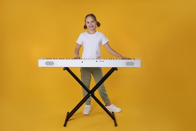 Photo of Cute girl playing synthesizer on orange background