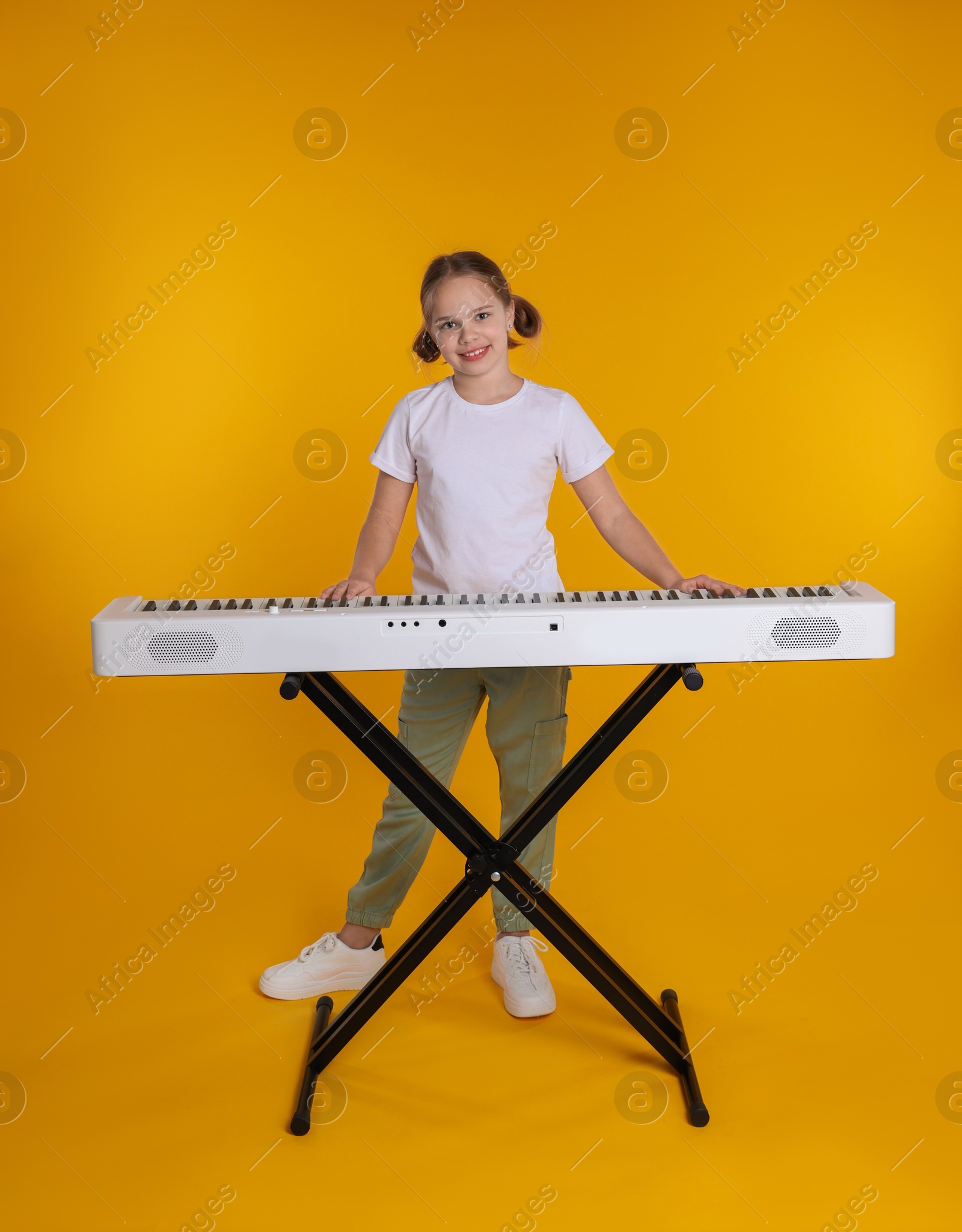 Photo of Cute girl playing synthesizer on orange background