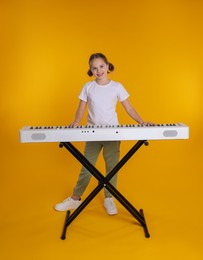 Cute girl playing synthesizer on orange background