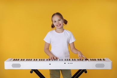 Photo of Cute girl playing synthesizer on orange background