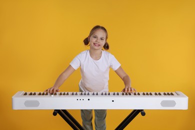 Photo of Cute girl playing synthesizer on orange background