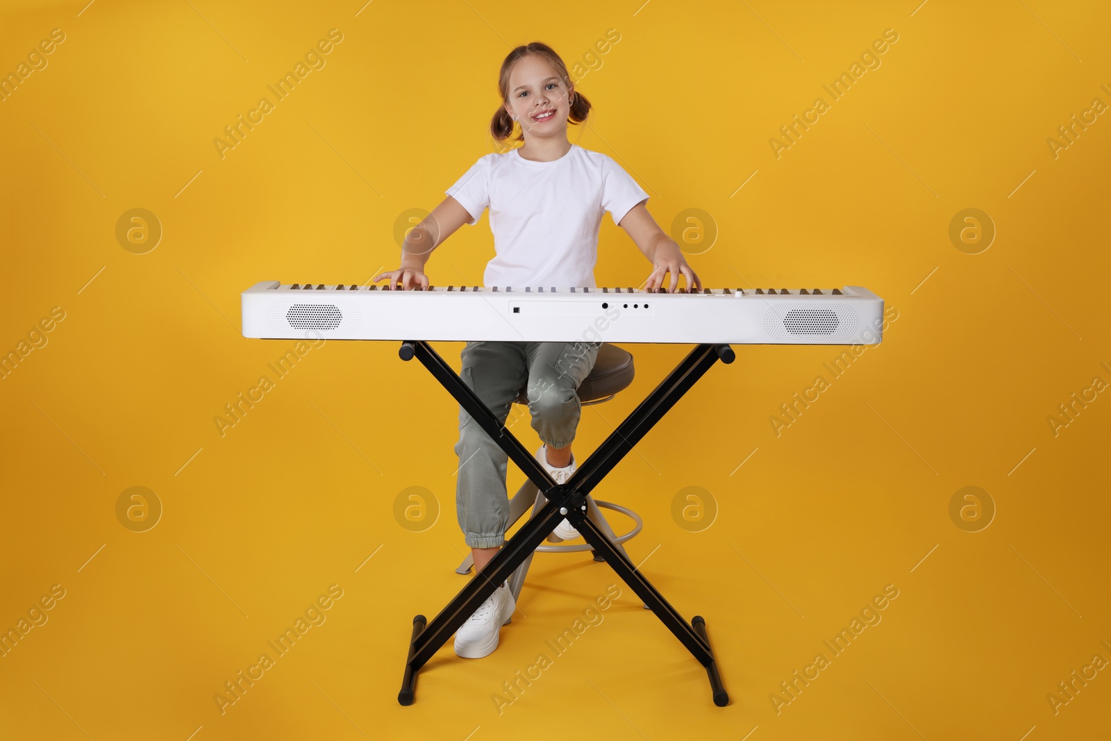 Photo of Cute girl playing synthesizer on orange background