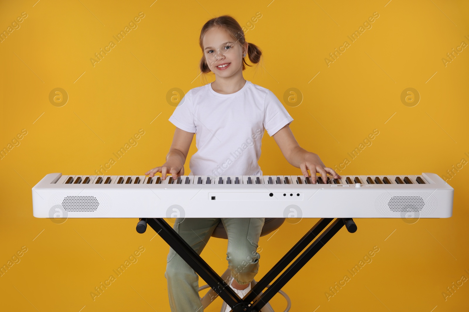 Photo of Cute girl playing synthesizer on orange background