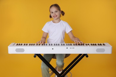 Photo of Cute girl playing synthesizer on orange background