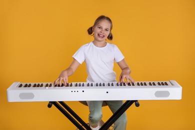 Photo of Cute girl playing synthesizer on orange background