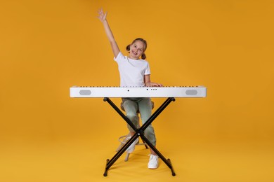 Photo of Cute girl playing synthesizer on orange background