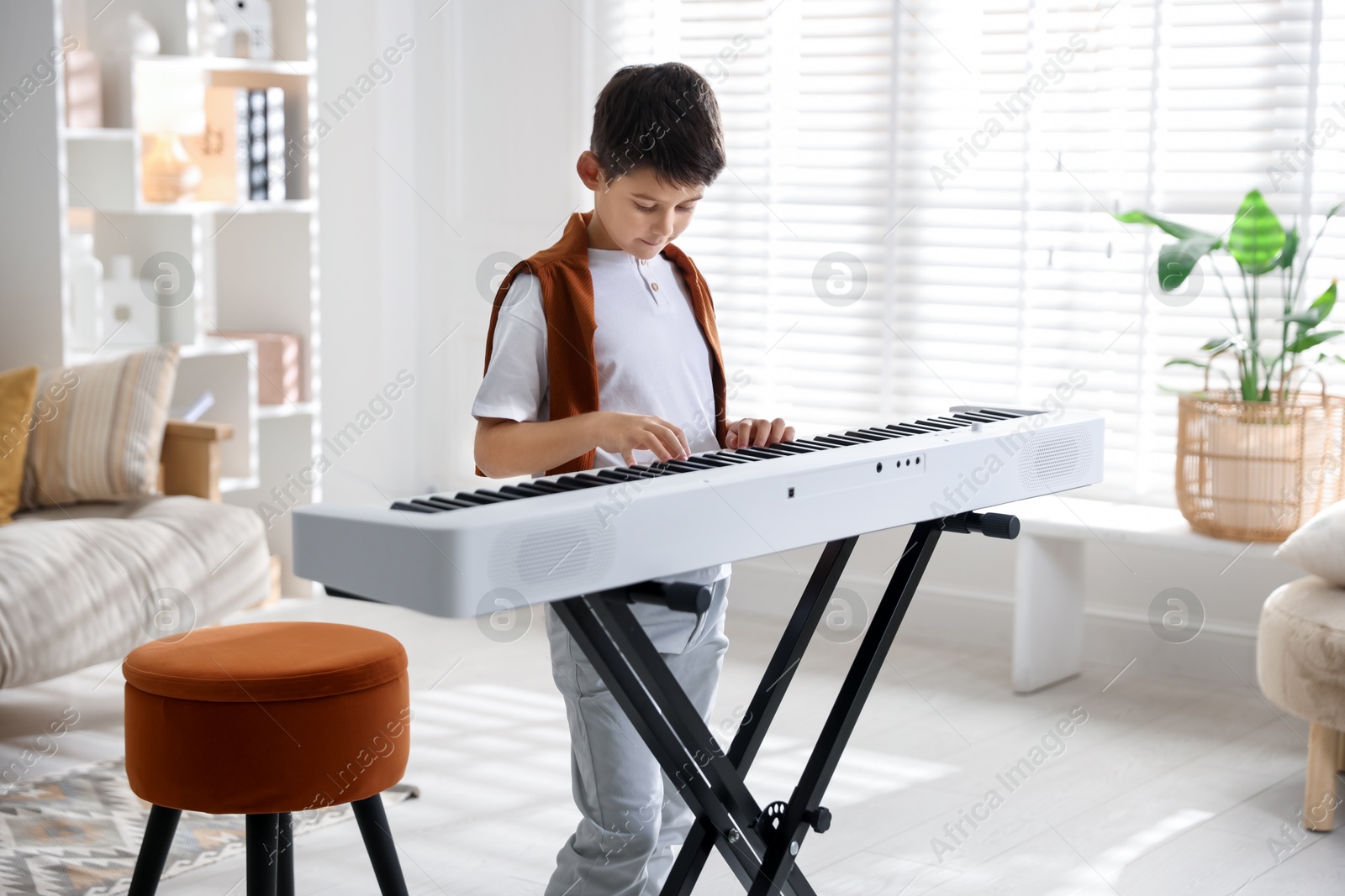 Photo of Cute boy playing synthesizer at home. Electronic musical instrument