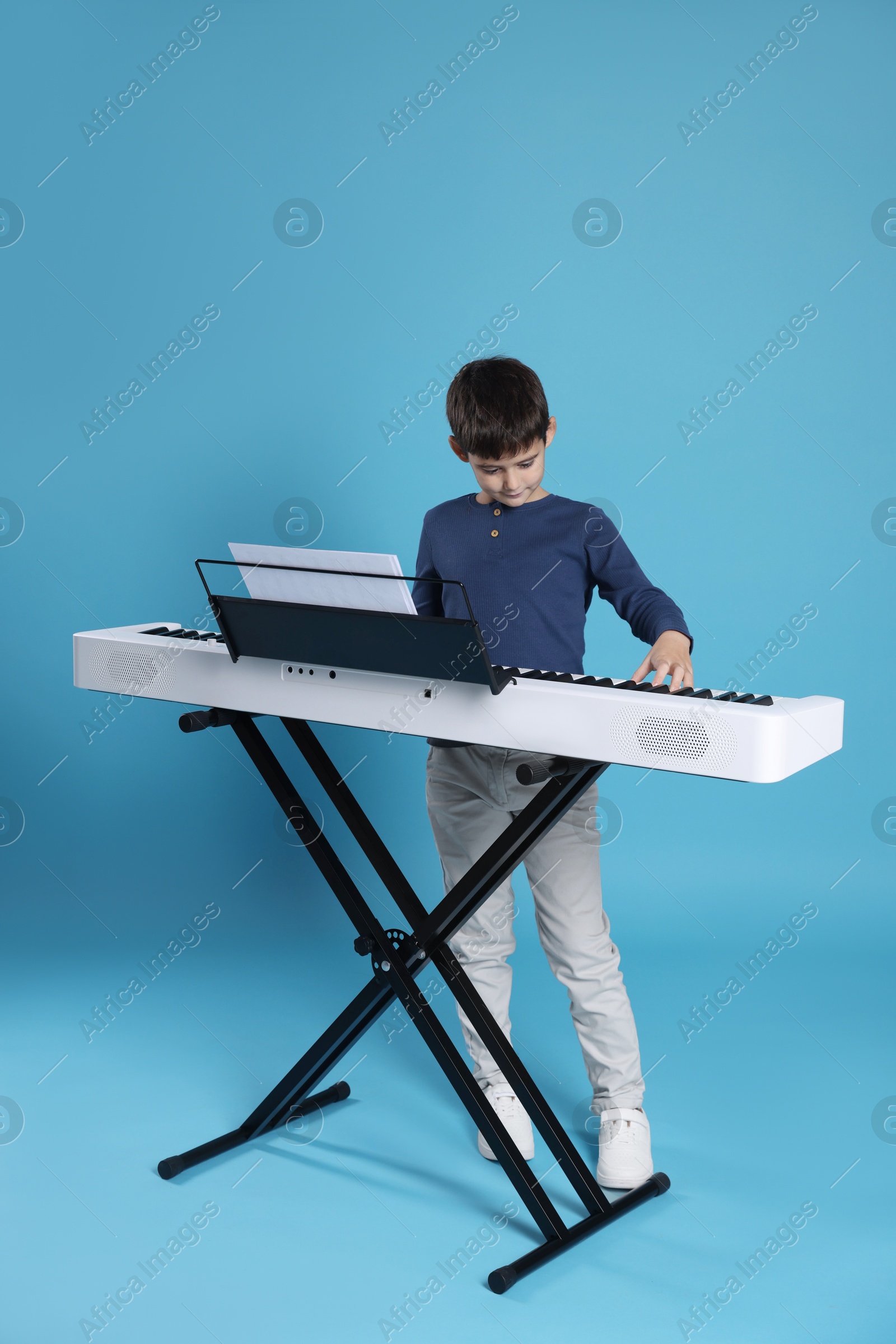 Photo of Cute boy playing synthesizer on light blue background