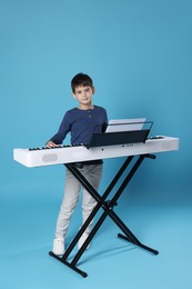 Photo of Cute boy playing synthesizer on light blue background