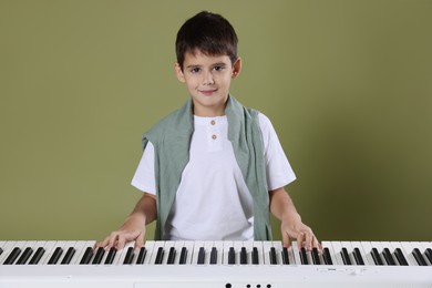 Photo of Cute boy playing synthesizer on olive background