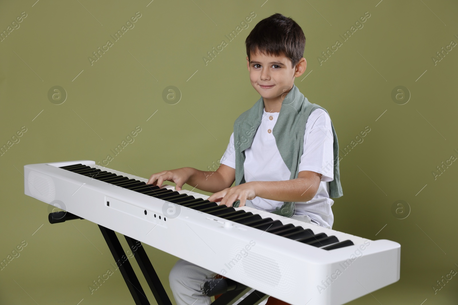 Photo of Cute boy playing synthesizer on olive background