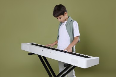 Photo of Cute boy playing synthesizer on olive background