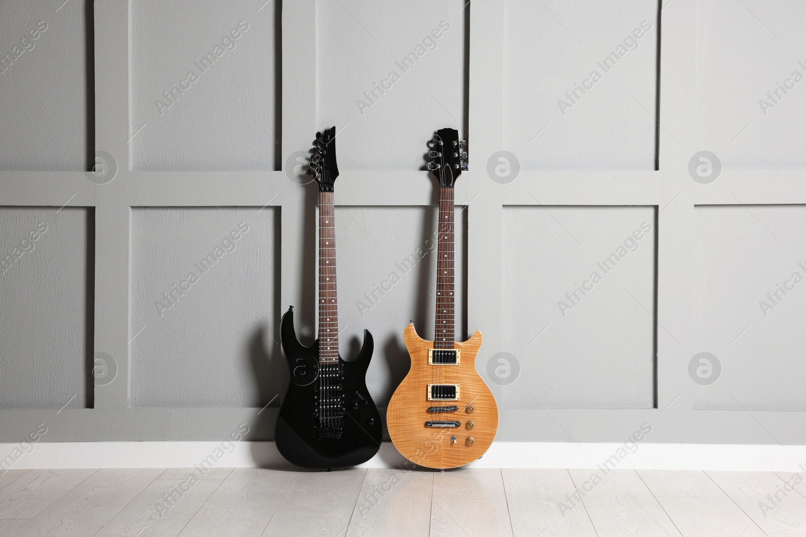 Photo of Two modern electric guitars near grey wall