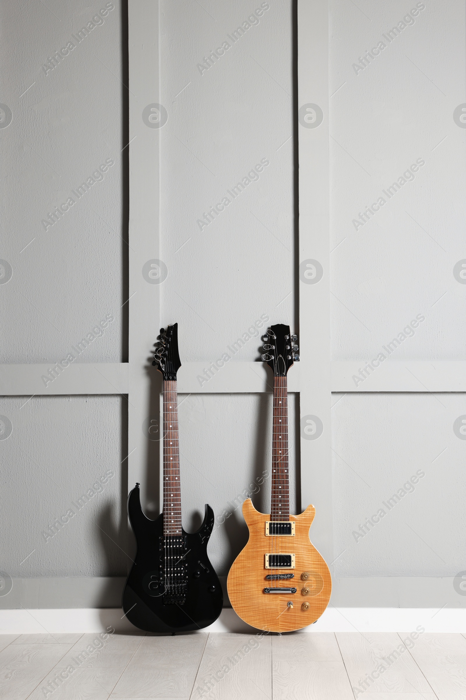 Photo of Two modern electric guitars near grey wall