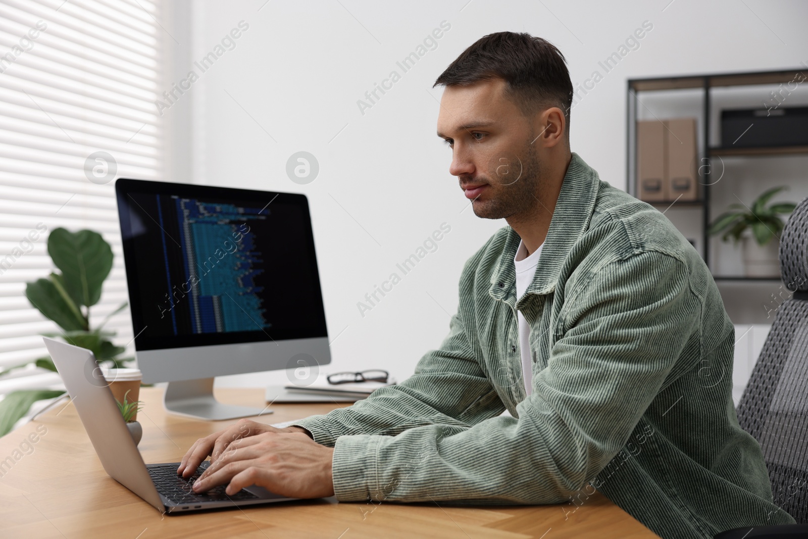 Photo of Programmer working on laptop at wooden desk indoors