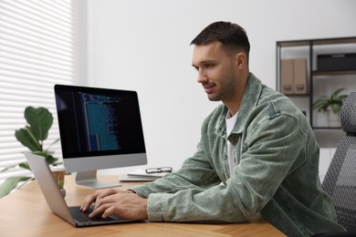 Photo of Programmer working on laptop at wooden desk indoors