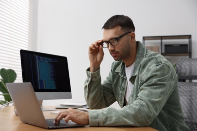 Photo of Programmer working on laptop at wooden desk indoors