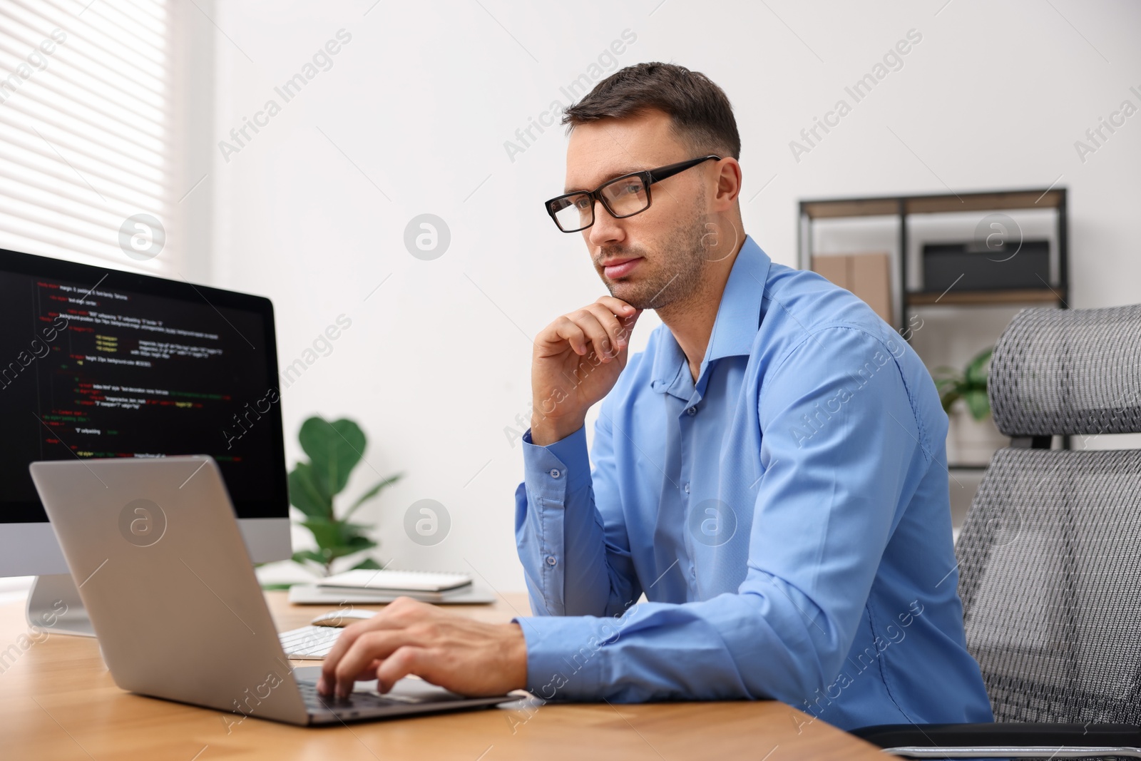 Photo of Programmer working on laptop at wooden desk indoors