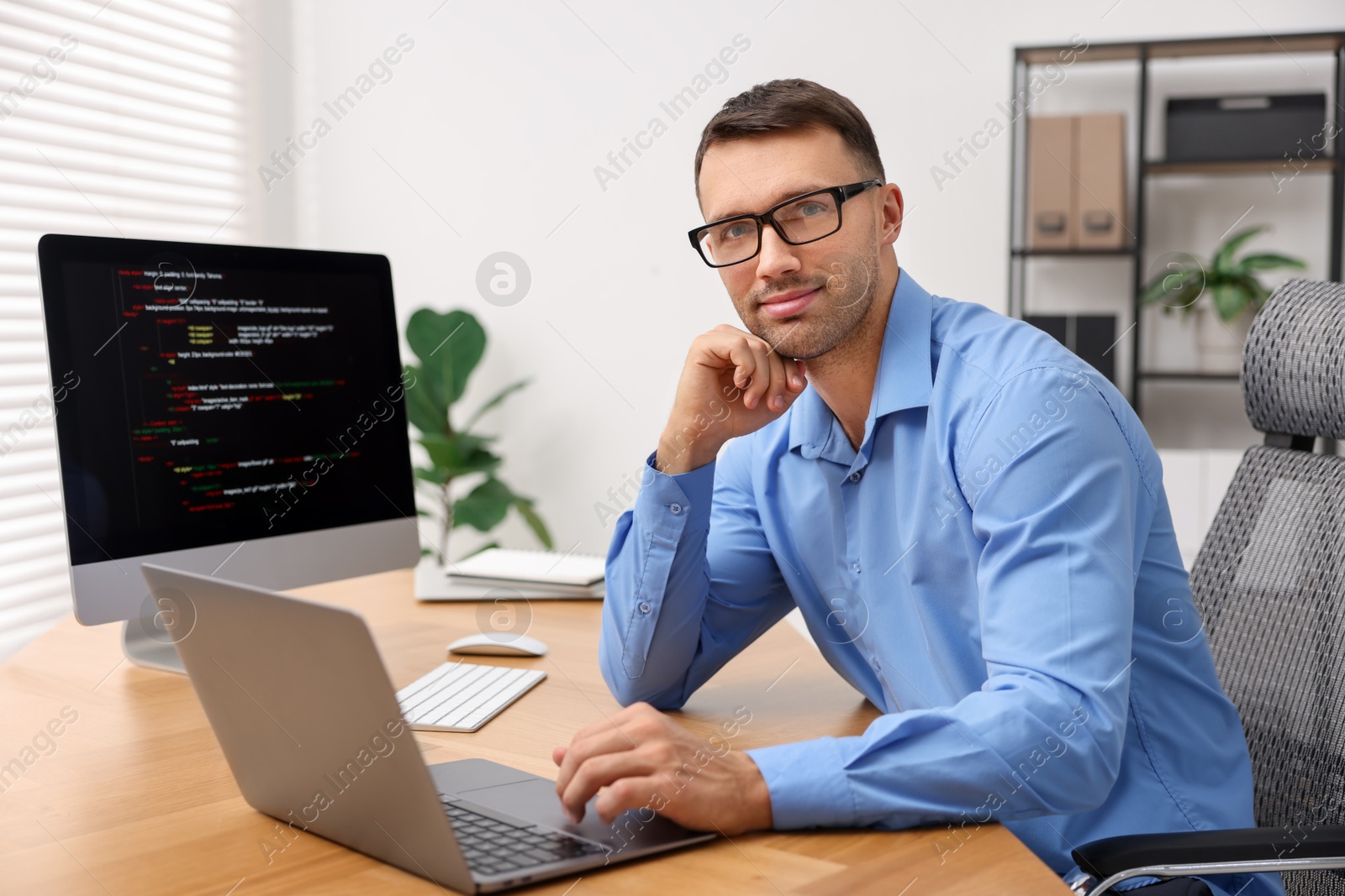 Photo of Programmer with laptop at wooden desk indoors