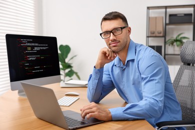 Photo of Programmer with laptop at wooden desk indoors