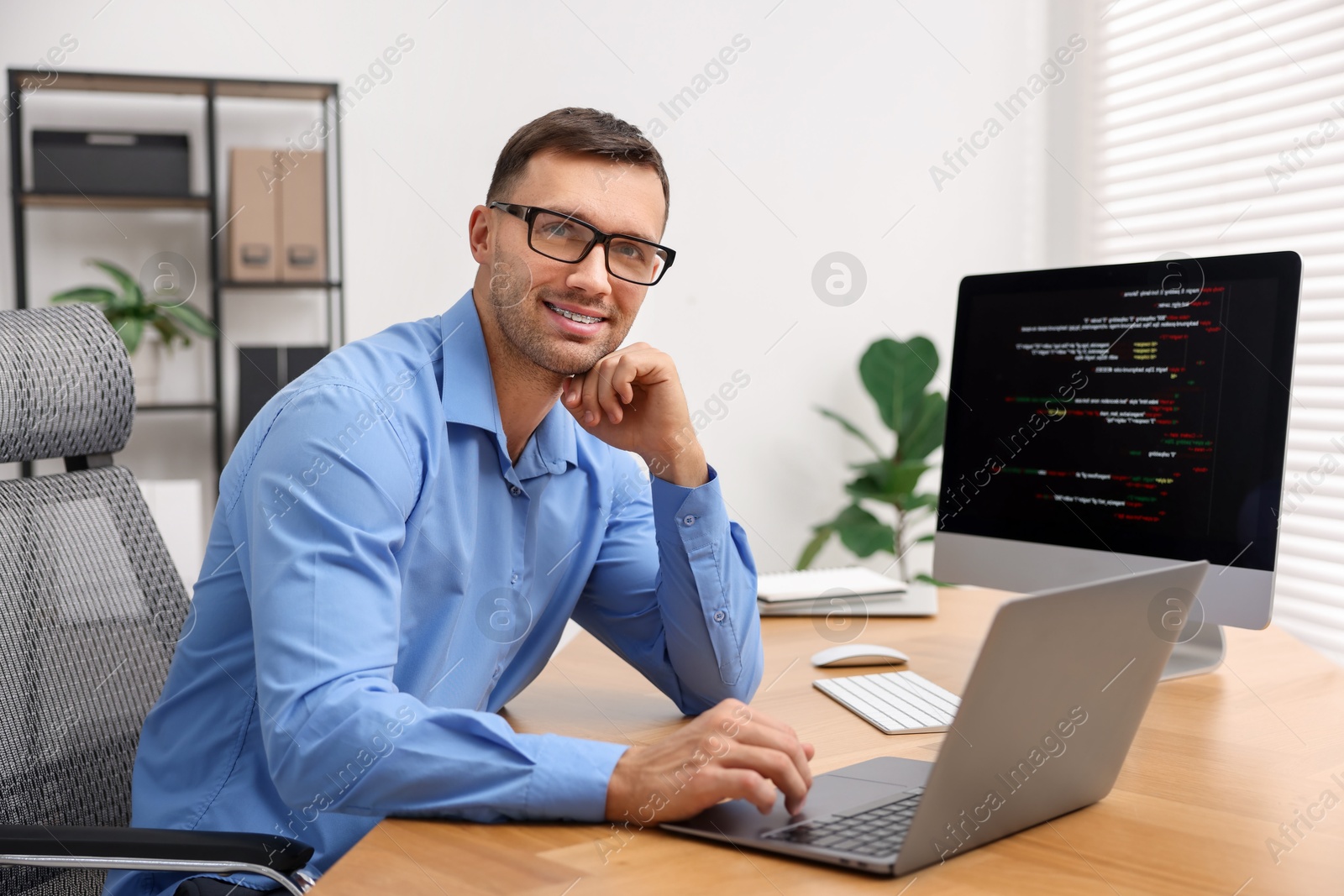 Photo of Programmer with laptop at wooden desk indoors