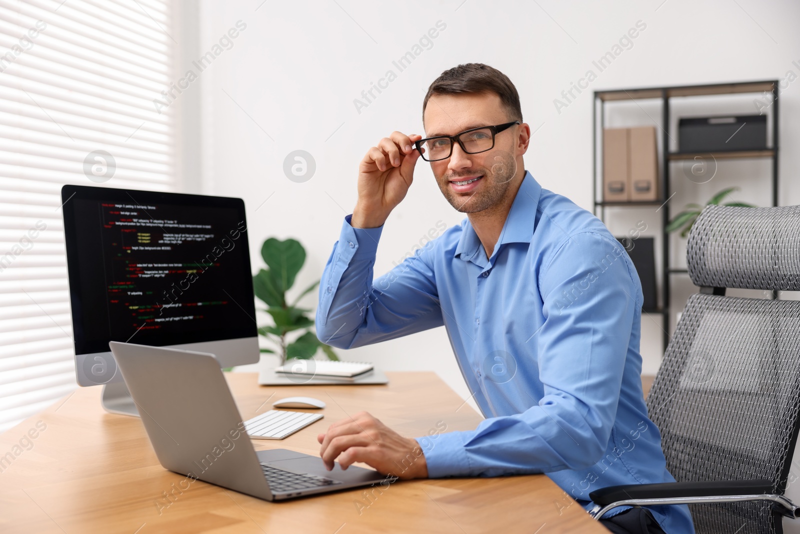 Photo of Programmer with laptop at wooden desk indoors