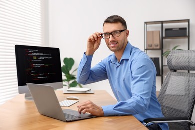 Photo of Programmer with laptop at wooden desk indoors