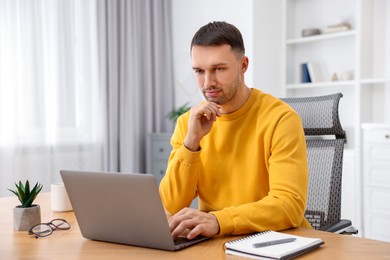 Photo of Programmer working on laptop at wooden desk indoors