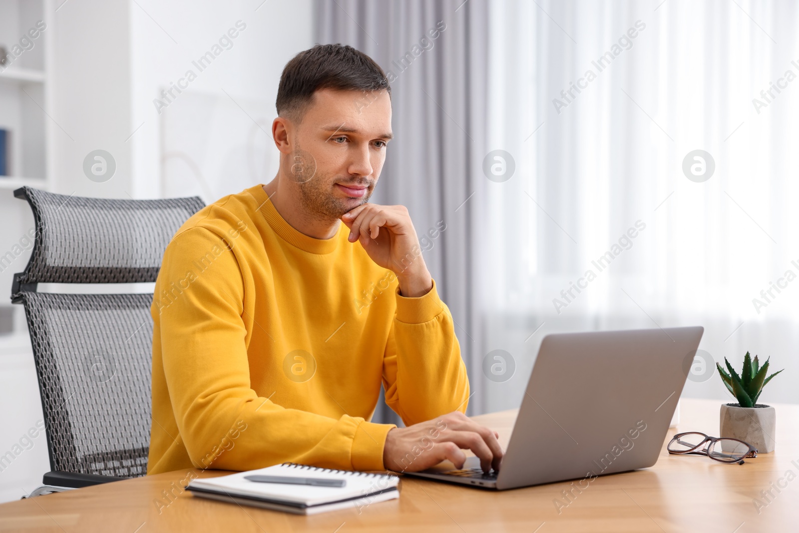 Photo of Programmer working on laptop at wooden desk indoors