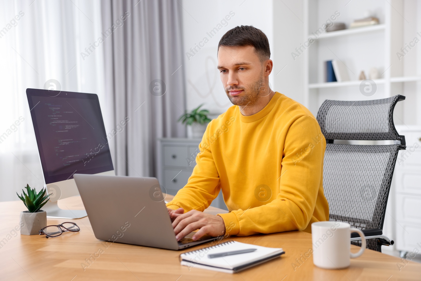 Photo of Programmer working on laptop at wooden desk indoors