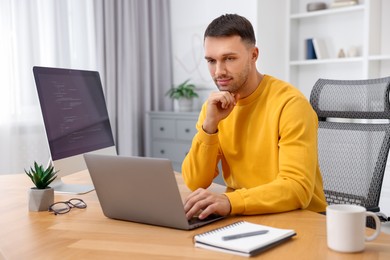 Photo of Programmer working on laptop at wooden desk indoors