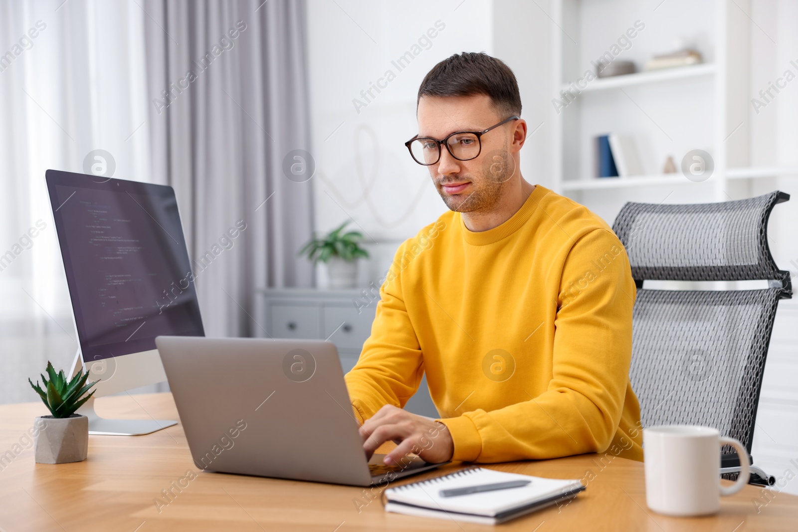 Photo of Programmer working on laptop at wooden desk indoors