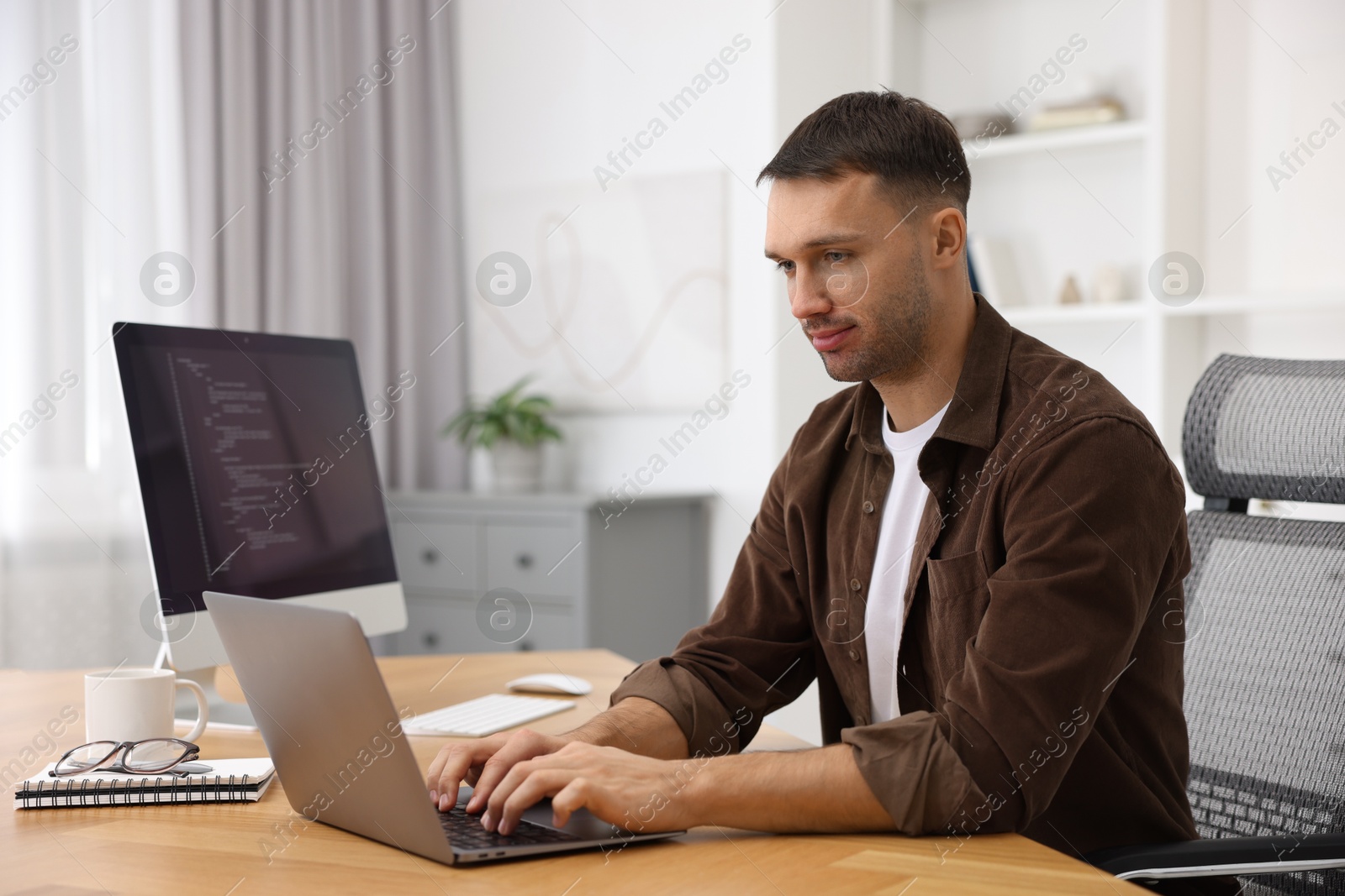 Photo of Programmer working on laptop at wooden desk indoors