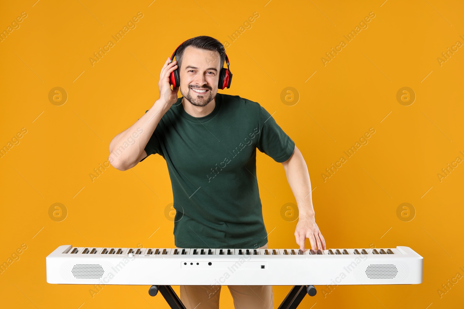 Photo of Smiling man in headphones playing synthesizer on orange background